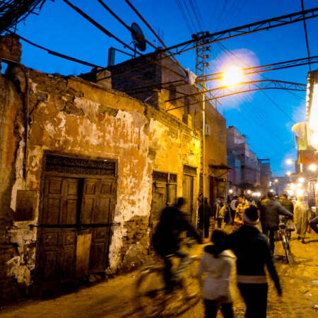 <p>Strollers and cyclists pass a dilapidated building in a Marrakech side street.</p>